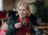 A woman enjoying a day out with a friend in Beadnell, North East England and they are sitting in a restaurant, taking a break from exploring the area. The main focus is the woman enjoying her hot drink while looking at her friend who is out of shot.