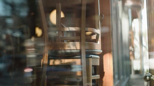 Curved glass window of a restaurant that is closed. Chairs are stacked on the tables.