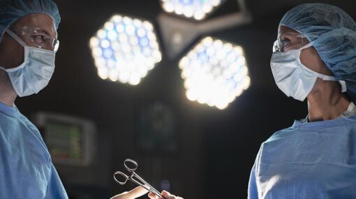 Side view of medical professionals doctor nurse surgeon passing surgical tool by hand to each other in operation surgery room in hospital as team teamwork back lit