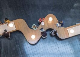 Panoramic overhead view of several business meetings going on in the communal area of a modern office building.