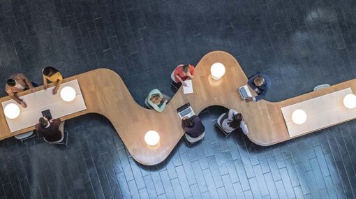 Panoramic overhead view of several business meetings going on in the communal area of a modern office building.